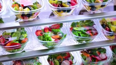 Önceden paketlenmiş meyve ve sebze salatalarıyla dolu plastik kutular ticari bir buzdolabında satılıyor.