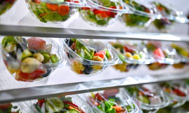 Önceden paketlenmiş meyve ve sebze salatalarıyla dolu plastik kutular ticari bir buzdolabında satılıyor.