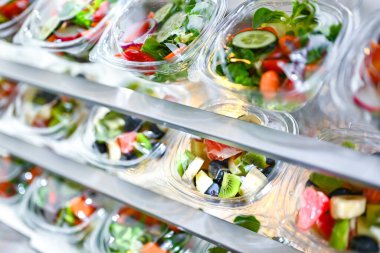 Önceden paketlenmiş meyve ve sebze salatalarıyla dolu plastik kutular ticari bir buzdolabında satılıyor.