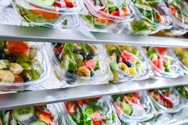 Önceden paketlenmiş meyve ve sebze salatalarıyla dolu plastik kutular ticari bir buzdolabında satılıyor.