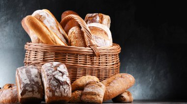 Hasır sepet içinde çeşitli fırın ürünleri ve ekmek ve rulo ekmekler var.