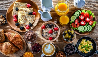 Kahvaltının yanında kahve, portakal suyu, kruvasan, mısır gevreği, çırpılmış yumurta ve krep var..