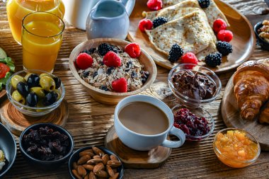 Kahvaltının yanında kahve, portakal suyu, kruvasan, mısır gevreği, çırpılmış yumurta ve krep var..