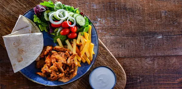 Patates kızartması, pitta ekmeği, sebze ve tzatziki ile servis edilir.