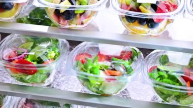 Önceden paketlenmiş meyve ve sebze salatalarıyla dolu plastik kutular ticari bir buzdolabında satılıyor.