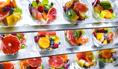 Plastic boxes with pre-packaged fruit salads, put up for sale in a commercial refrigerator clipart