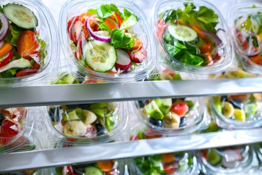Önceden paketlenmiş meyve ve sebze salatalarıyla dolu plastik kutular ticari bir buzdolabında satılıyor.