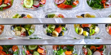 Önceden paketlenmiş meyve ve sebze salatalarıyla dolu plastik kutular ticari bir buzdolabında satılıyor.