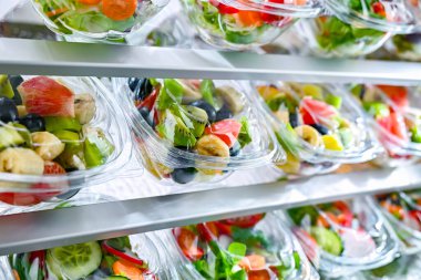 Önceden paketlenmiş meyve ve sebze salatalarıyla dolu plastik kutular ticari bir buzdolabında satılıyor.