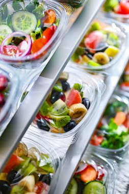 Önceden paketlenmiş meyve ve sebze salatalarıyla dolu plastik kutular ticari bir buzdolabında satılıyor.
