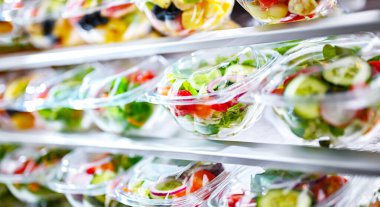 Önceden paketlenmiş meyve ve sebze salatalarıyla dolu plastik kutular ticari bir buzdolabında satılıyor.