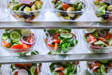 Önceden paketlenmiş meyve ve sebze salatalarıyla dolu plastik kutular ticari bir buzdolabında satılıyor.