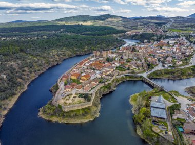 Madrid yakınlarındaki iyi korunmuş tarihi bir köy olan Buitrago del Lozoya 'nın havadan görünüşü, arkasında Guadarrama dağ zinciri ve rezervuar bulunan Lozoya nehri ile çevrilidir. Uzun pozlama.