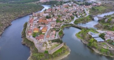 Madrid yakınlarındaki iyi korunmuş tarihi bir köy olan Buitrago del Lozoya 'nın havadan görünüşü, arkasında Guadarrama dağ zinciri ve rezervuar bulunan Lozoya nehri ile çevrilidir. Uzun pozlama.