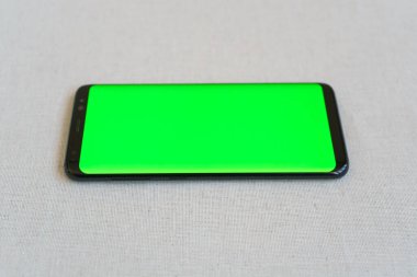 Cep telefonu yeşil ekranlı yatay olarak masada.