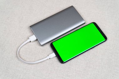 Smartphone with green screen charging with silver power bank.