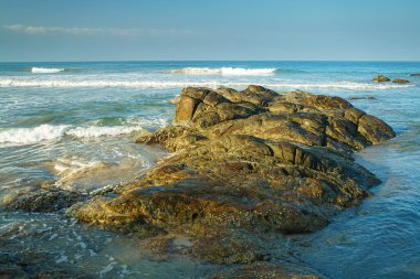 A large stone in the water near the ocean.