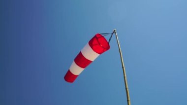 Windsock flutters showing wind direction against blue sky.