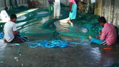 Mans are sitting on the floor with preparing a fishing net.