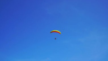 Mavi gökyüzünde motorlu bir paraglider uçar.
