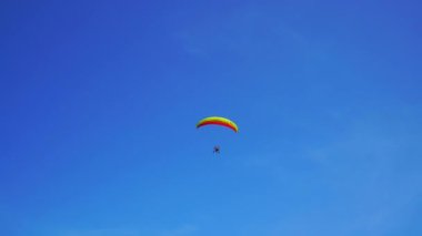 Mavi gökyüzünde motorlu bir paraglider uçar.