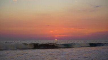 Güneş ufuktan batıyor dalgalarla dolu bir sahilde..