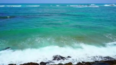 Mavi okyanus dalgaları kıyıdaki büyük taşlara vuruyor..