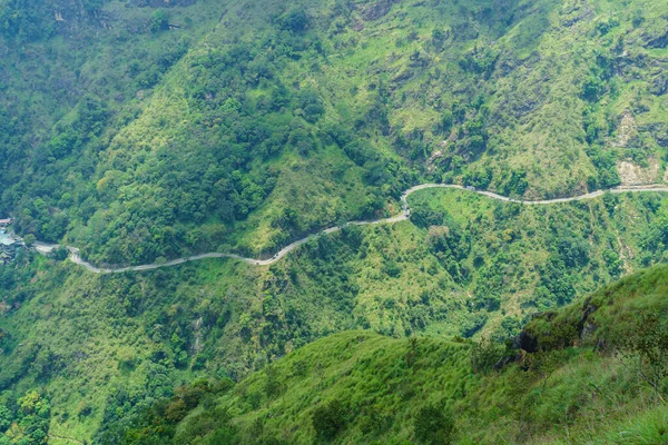 Dağ yolu yeşil bitki örtüsüyle kaplı dağın yamacından geçiyor..