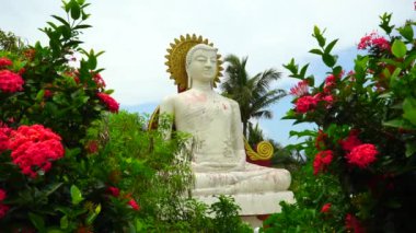 Çiçekler ve tropikal bitkiler arasında Buda heykeli.
