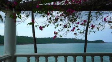 Bulutlu bir günde, balkondan çiçekli okyanus manzarası.