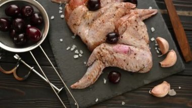 Raw chicken wings sprinkled with spices, red peppercorns and rosemary rotate slowly.
