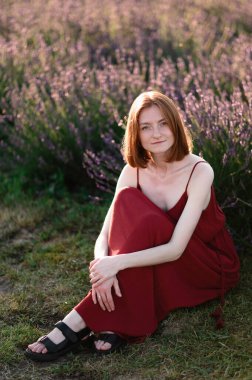 A red-haired young girl without make-up is resting in a lavender field. Summer vacation and travel time.