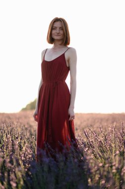 A red-haired young girl without make-up is resting in a lavender field. Summer vacation and travel time.