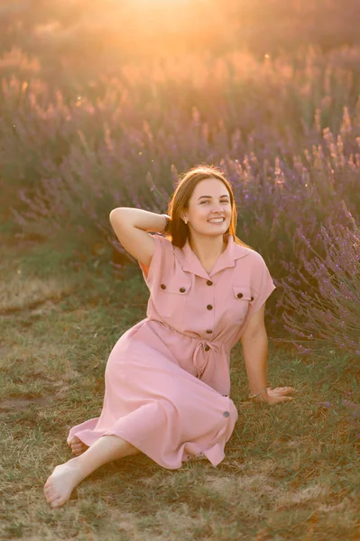 ピンクのドレスを着た明るい少女がラベンダーの茂みの中に座って休んでいます ストックフォト