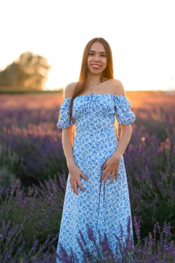 Attractive slender happy girl in a blue dress in a lavender field at sunset.