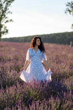 Portrait of a happy woman in a blue dress enjoying a sunny summer day in a lavender field. Fresh air, Lifestyle.