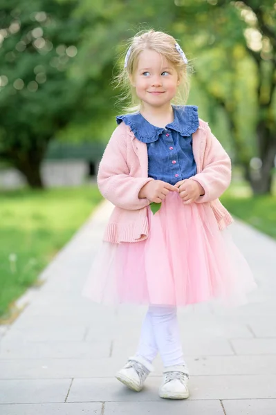 3歳の女の子がドレスとピンクのセーターで公園を歩いています 夏時間だ 赤ん坊は笑顔で目を背けている 少女は足を横切った — ストック写真