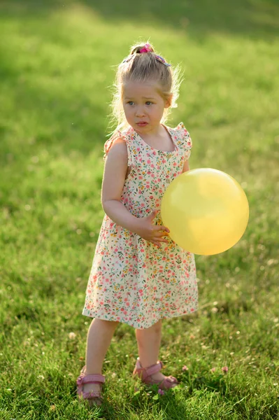 3岁的小女孩穿着夏装站在空地上 手里拿着一个黄色的球 这个女孩不开心 — 图库照片
