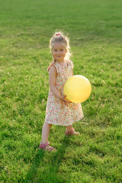 3岁的小女孩穿着夏装站在空地上 手里拿着一个黄色的球 这个女孩很开心 — 图库照片