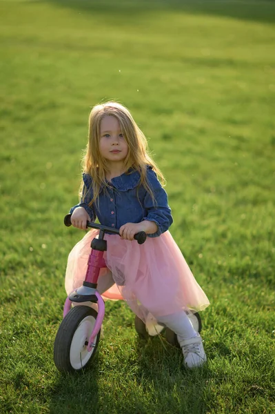幸せな美しい女の子は速く走り 暖かい夏の日に芝生の上でペダルなしで彼女の最初の自転車に乗ります かわいい赤ちゃん3歳 サイドビュー バランスを保つことを学ぶ ストックフォト