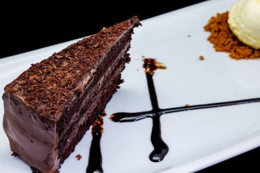 Beyaz tabakta çikolatalı pasta ve siyah arka planda dondurma kompozisyonu.
