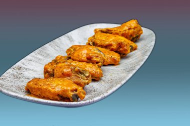 Morumsu ve açık mavi arka planda Bufalo soslu tavuk kanadı kompozisyonu.