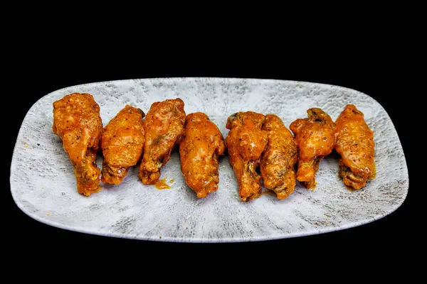 Composition of a plate of chicken wings with Buffalo sauce on a black background.