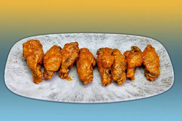 Composition of a plate of chicken wings with Buffalo sauce on a yellow and light blue background