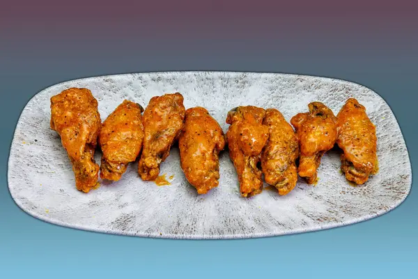 Composition of a plate of chicken wings with Buffalo sauce on a magenta and light blue background.