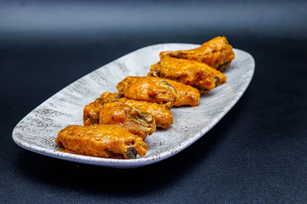 Composition of a plate of chicken wings with Buffalo sauce on a black background.
