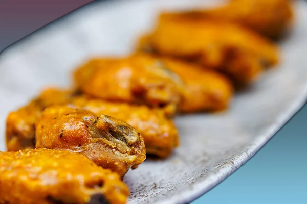 Composition of a plate of chicken wings with Buffalo sauce on a magenta and light blue background.