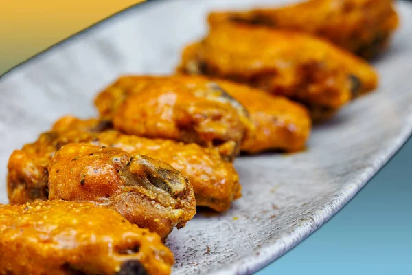 Composition of a plate of chicken wings with Buffalo sauce on a yellow and light blue background