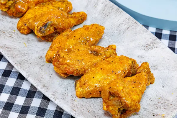 Composition of a plate of chicken wings with Buffalo sauce on a black and white checkered tablecloth.