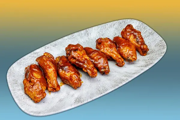 Composition of a plate of chicken wings with BBQ sauce on a yellow and light blue gradient background